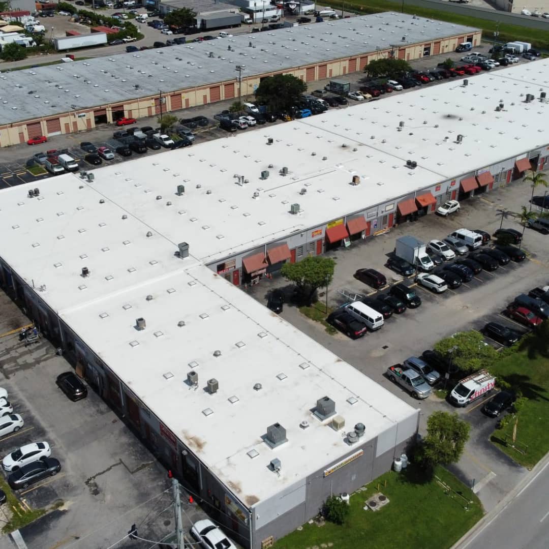 Aerial view of a commercial center with parking and multiple store entrances.
