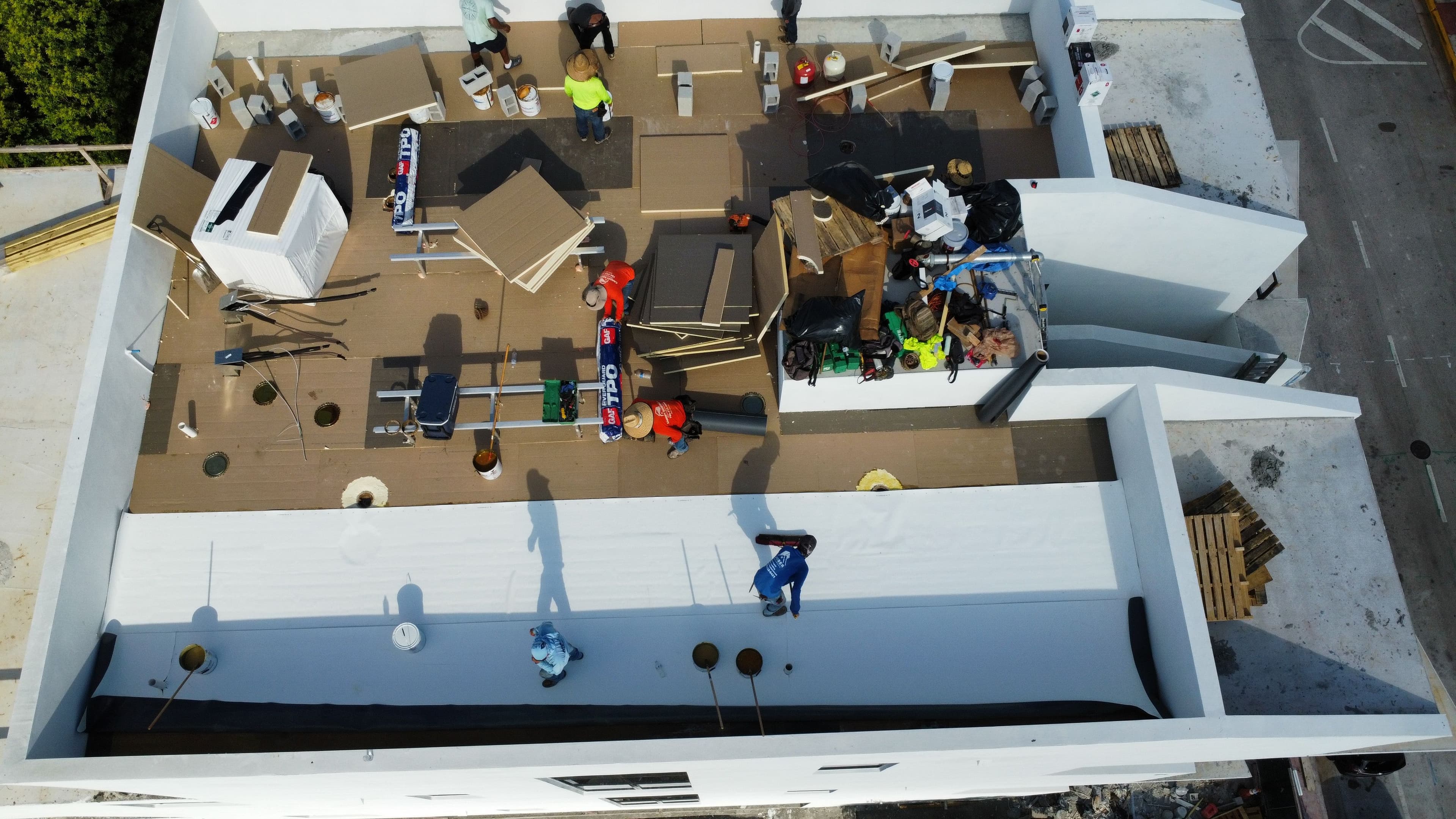 Aerial view of rooftop construction with workers applying materials and organizing tools.