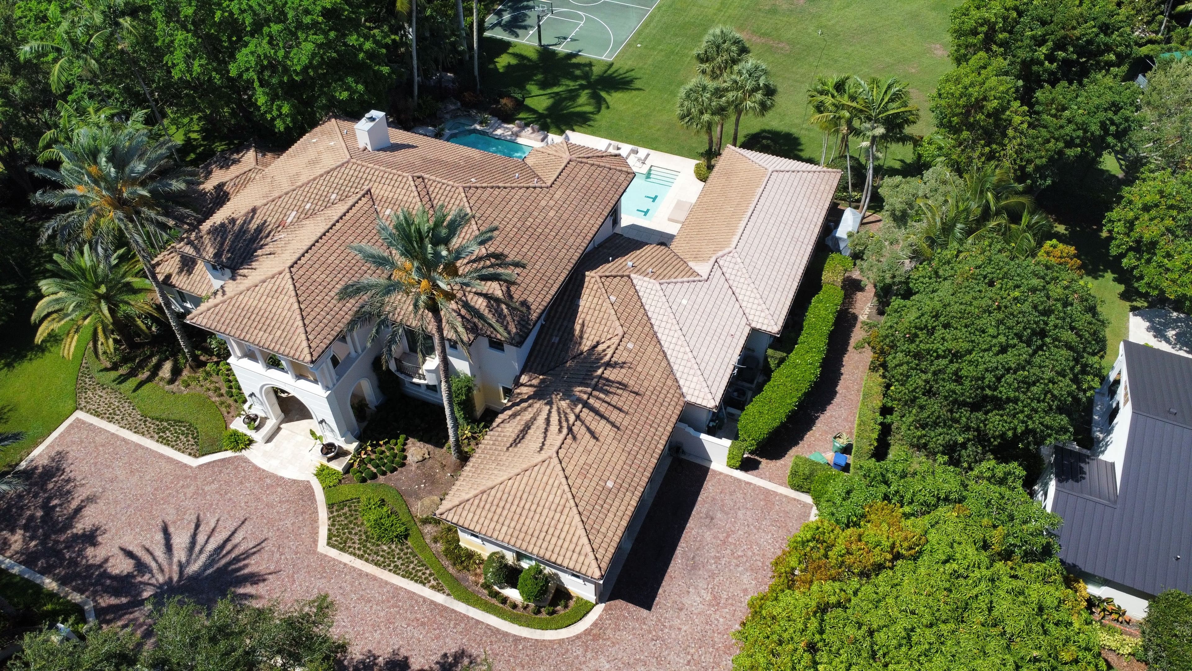 Aerial view of an elegant mansion with a pool, surrounded by lush greenery and palm trees.