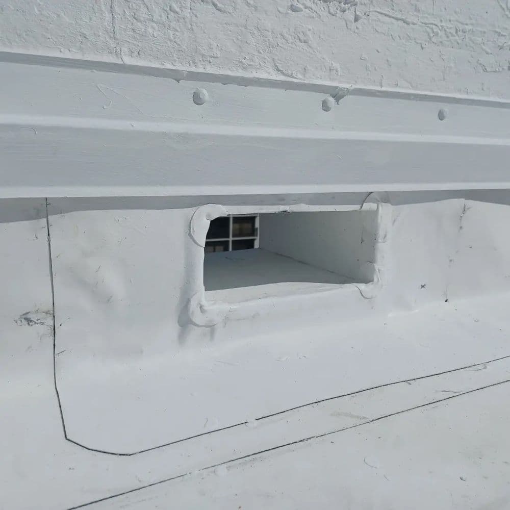 Roof ventilation opening with white sealant and metal trim on a flat roofing surface.