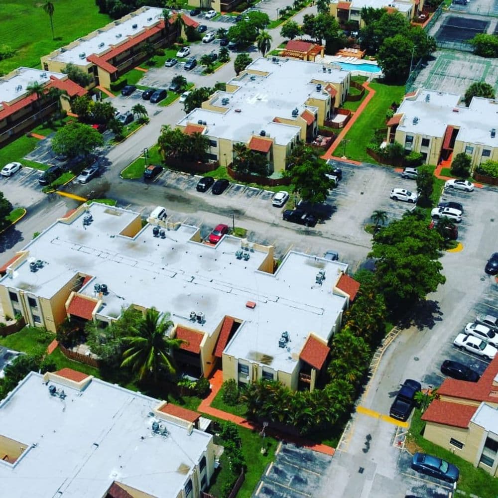 Aerial view of residential buildings and parking lot surrounded by greenery.