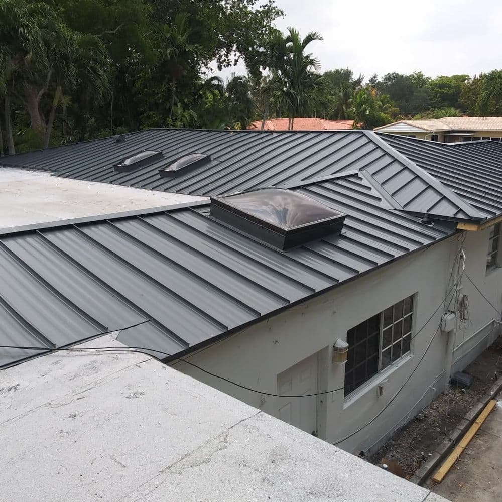 Metal roof installation on a residential building with skylights and surrounding greenery.