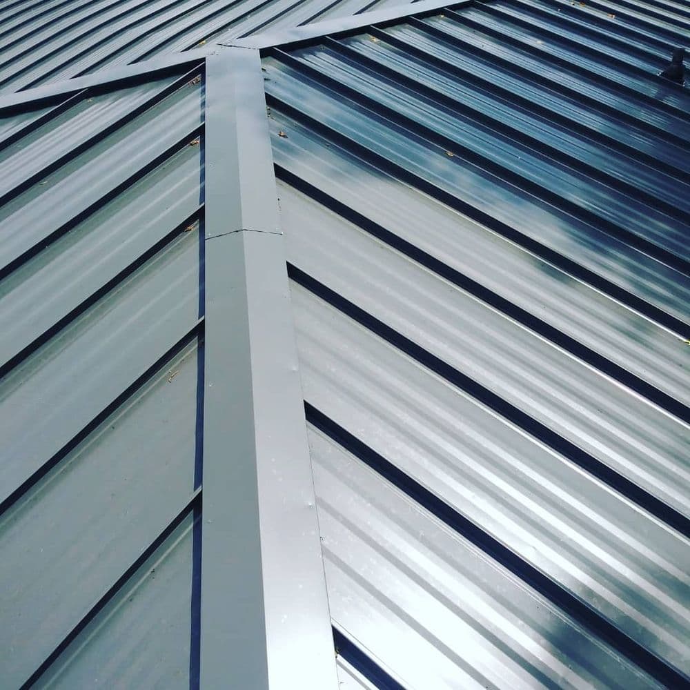 Metal roof with shiny, angled panels reflecting light under a clear sky.