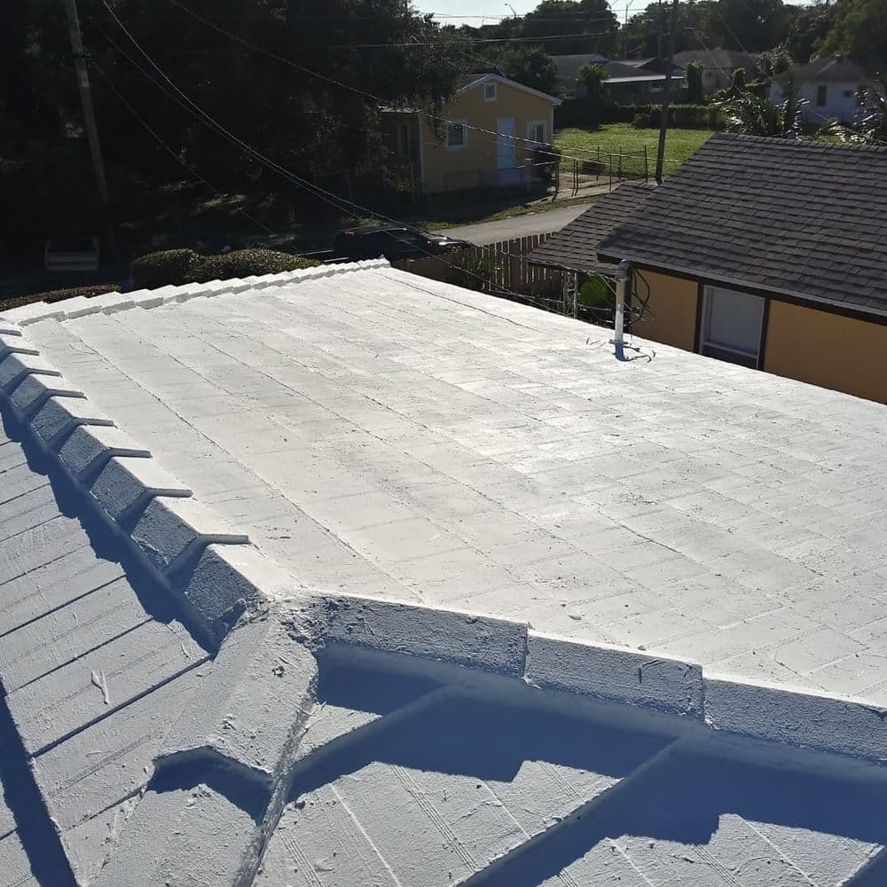 Flat white roof with textured surface, surrounded by residential buildings and greenery.