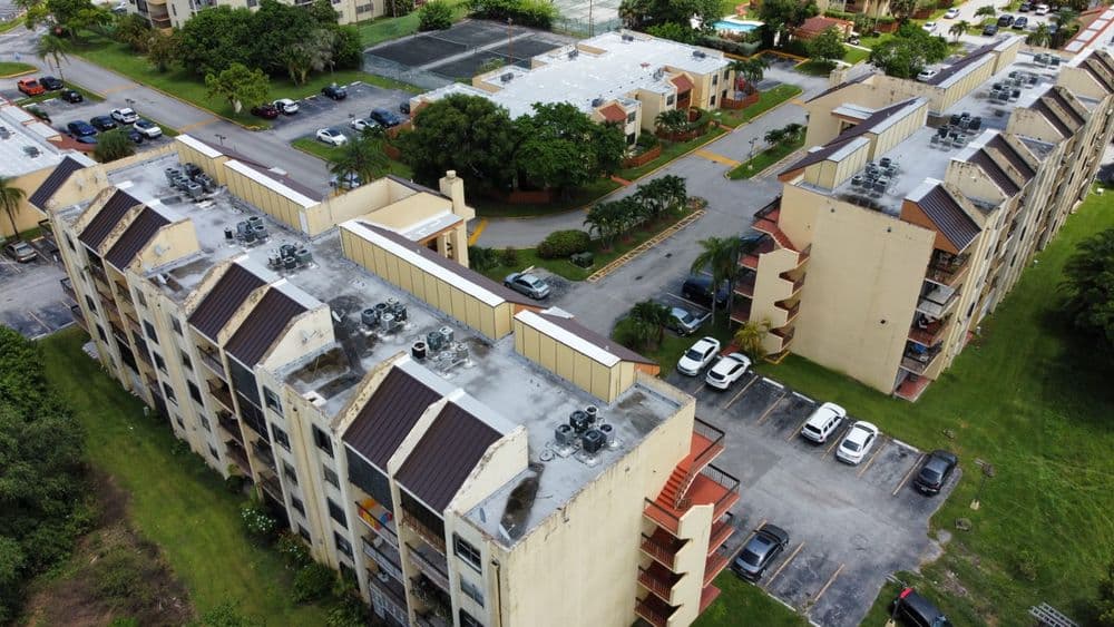 Aerial view of multi-story apartment buildings with rooftops and parking area in a residential complex.