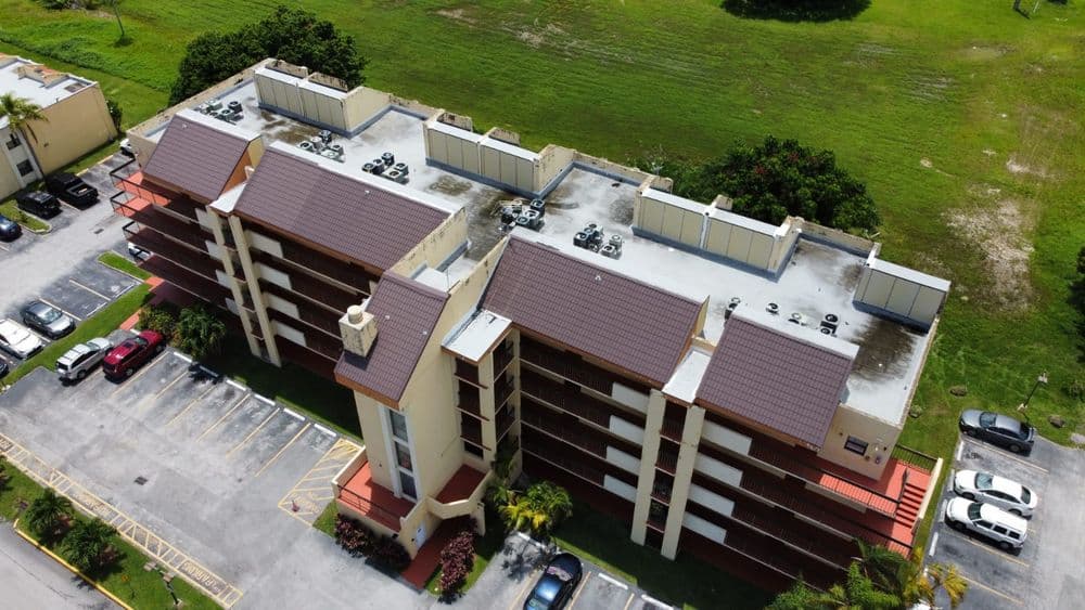 Aerial view of a multi-story apartment building with landscaped surroundings and parking lot.