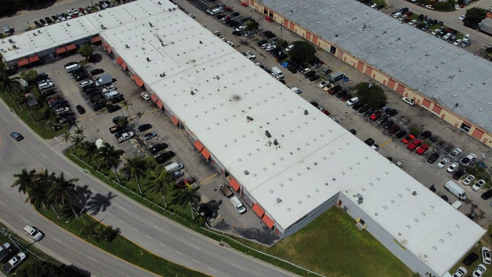 Aerial view of a large commercial building with parking lot and surrounding palm trees.