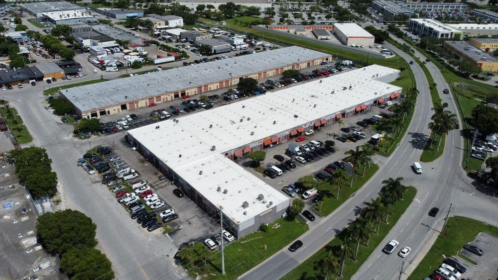 Aerial view of commercial buildings with parking lots and surrounding greenery.