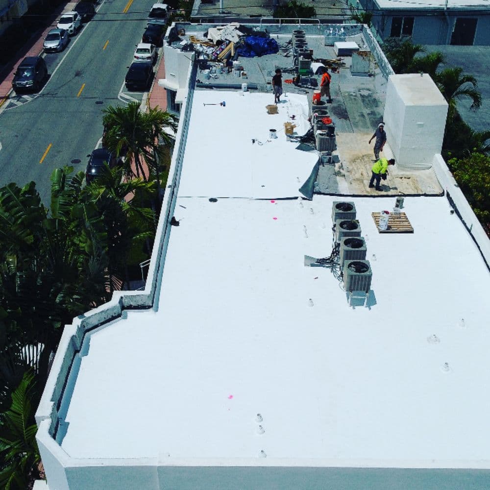 Roofing crew working on a flat white roof with HVAC units in a busy urban area.