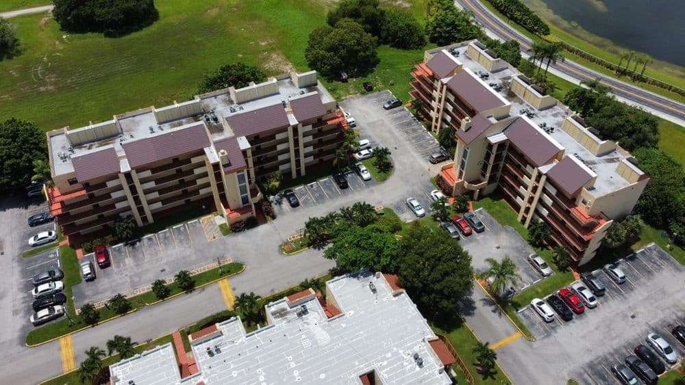 Aerial view of multi-story apartments with parking lot and greenery nearby.