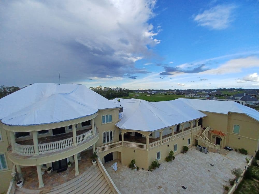 Luxury villa with white protective covering against a scenic blue sky and golf course backdrop.