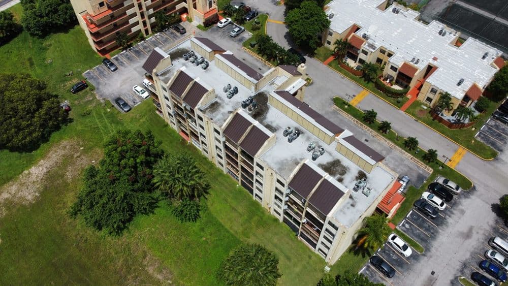 Aerial view of a residential building surrounded by greenery and parking lots.