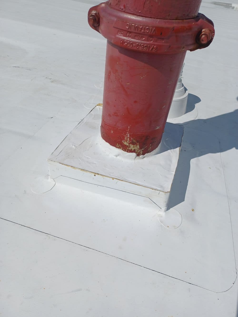 Red fire hydrant mounted on a white rooftop surface with protective base.