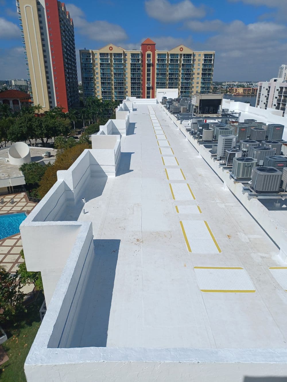 Aerial view of a rooftop with ventilation units and adjacent buildings against a blue sky.