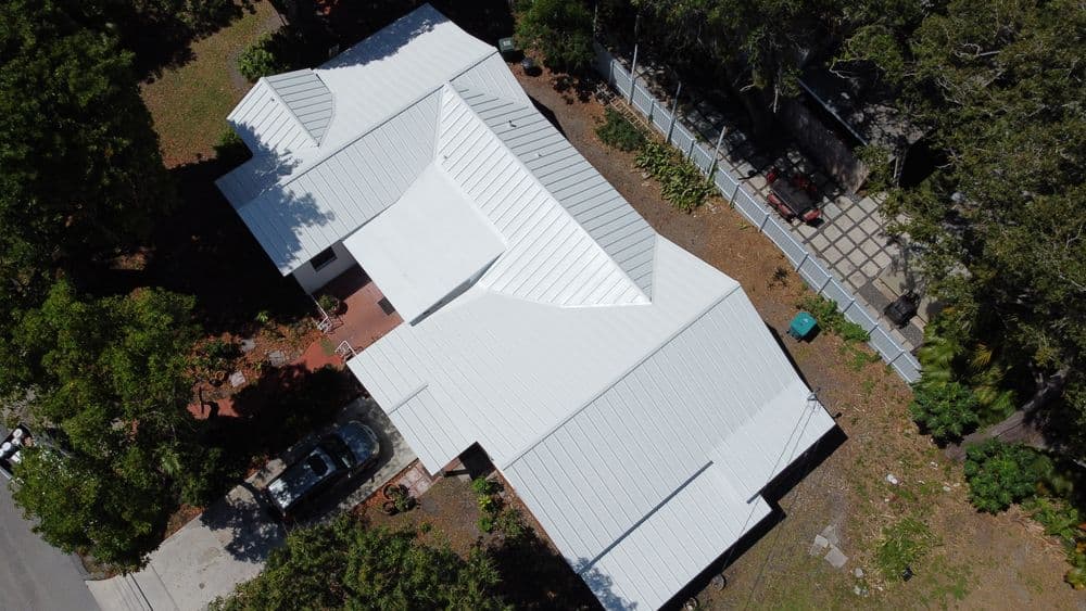 Aerial view of a modern white-roofed house surrounded by greenery and landscaped gardens.
