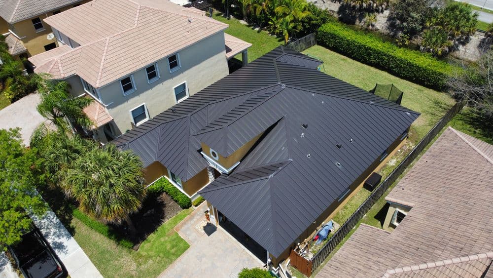 Aerial view of modern metal roof atop a residential house with landscaped yard.