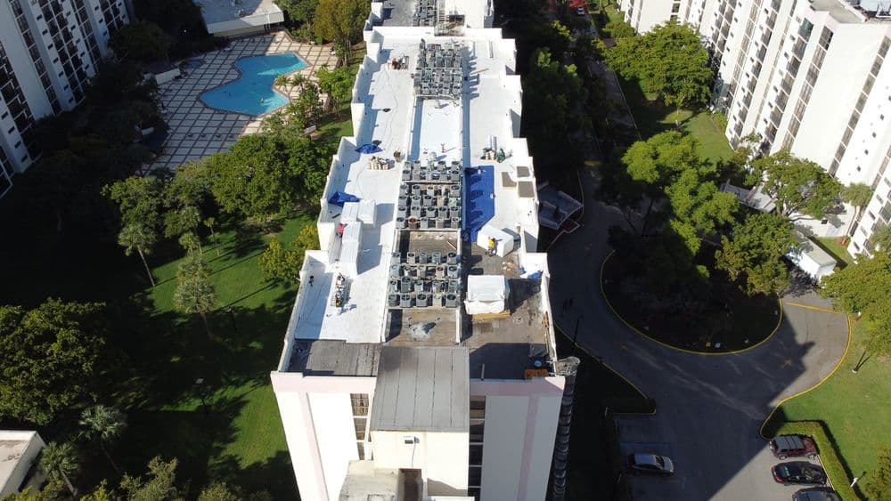 Aerial view of a building rooftop with air conditioning units and a pool in the background.