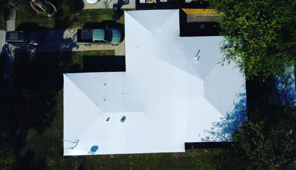 Aerial view of a residential home with a white roof and green lawn.