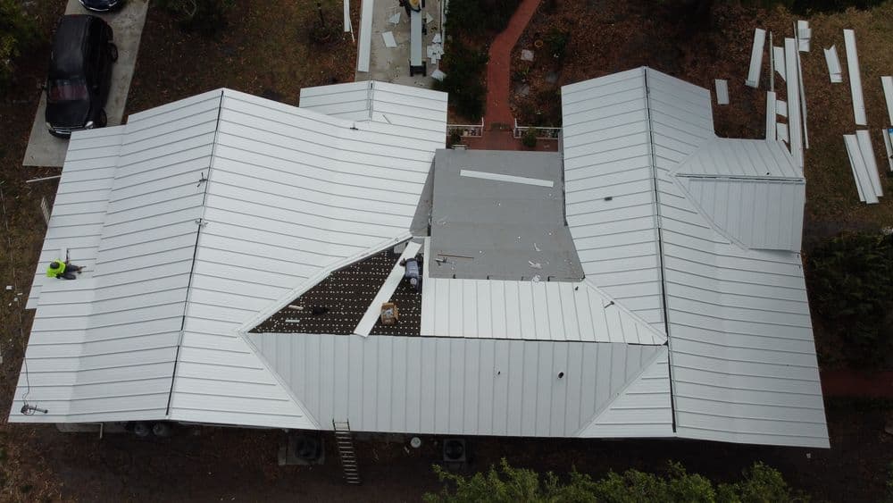 Aerial view of a house with a new metal roof installation in progress.