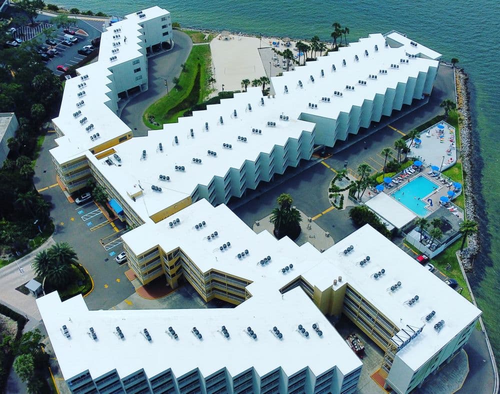 Aerial view of a modern beachfront hotel with a pool and palm trees near the shoreline.