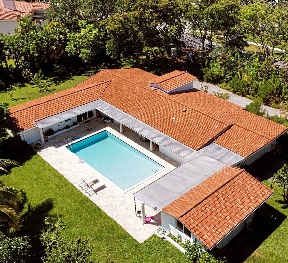Aerial view of a modern home with a pool surrounded by greenery and trees.