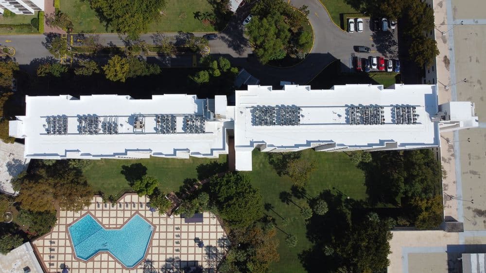 Aerial view of two buildings with rooftop HVAC units and a pool surrounded by greenery.