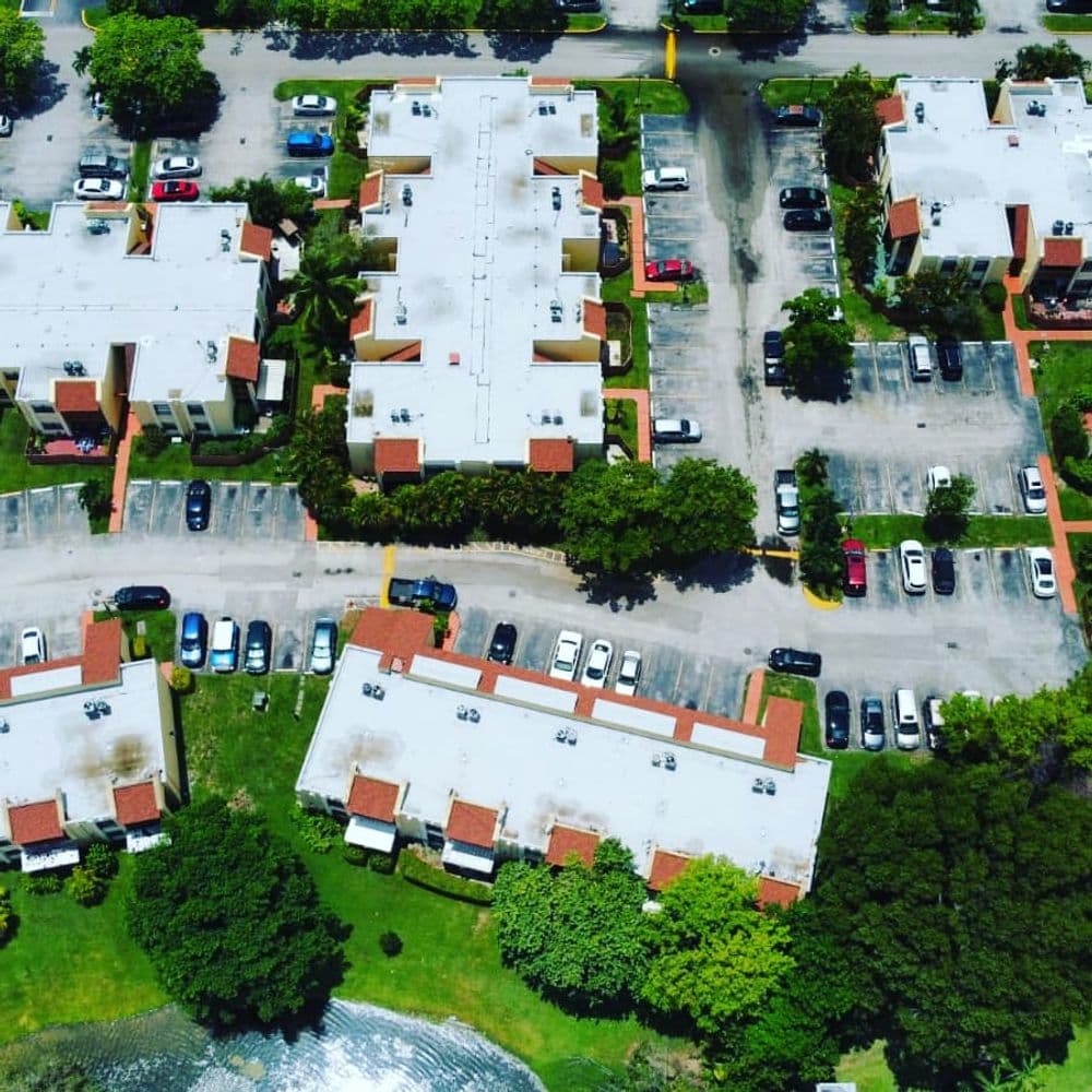 Aerial view of a residential complex with parking lots and greenery nearby.