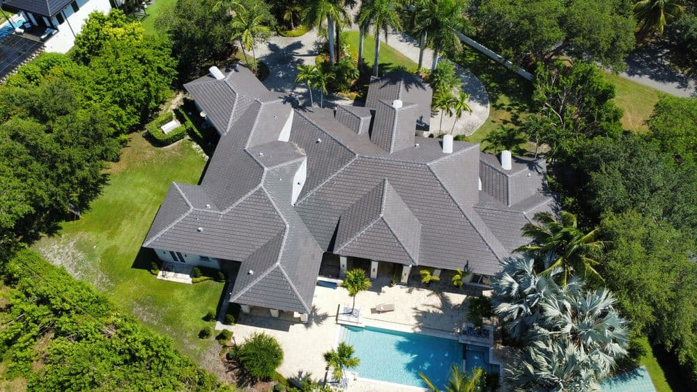 Aerial view of a luxurious home with a pool, surrounded by lush greenery and palm trees.