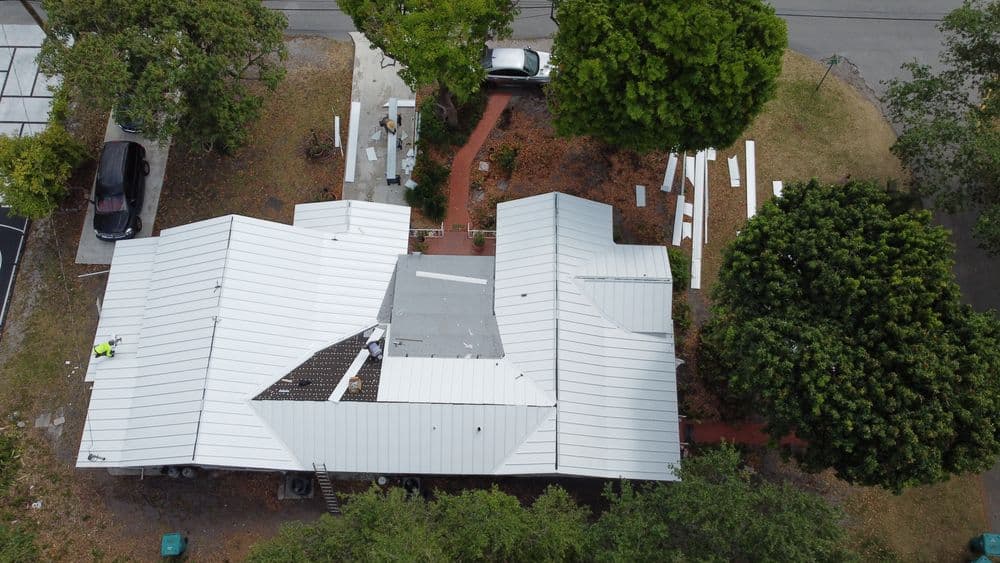 Aerial view of a modern home with a unique metal roof and surrounding greenery.