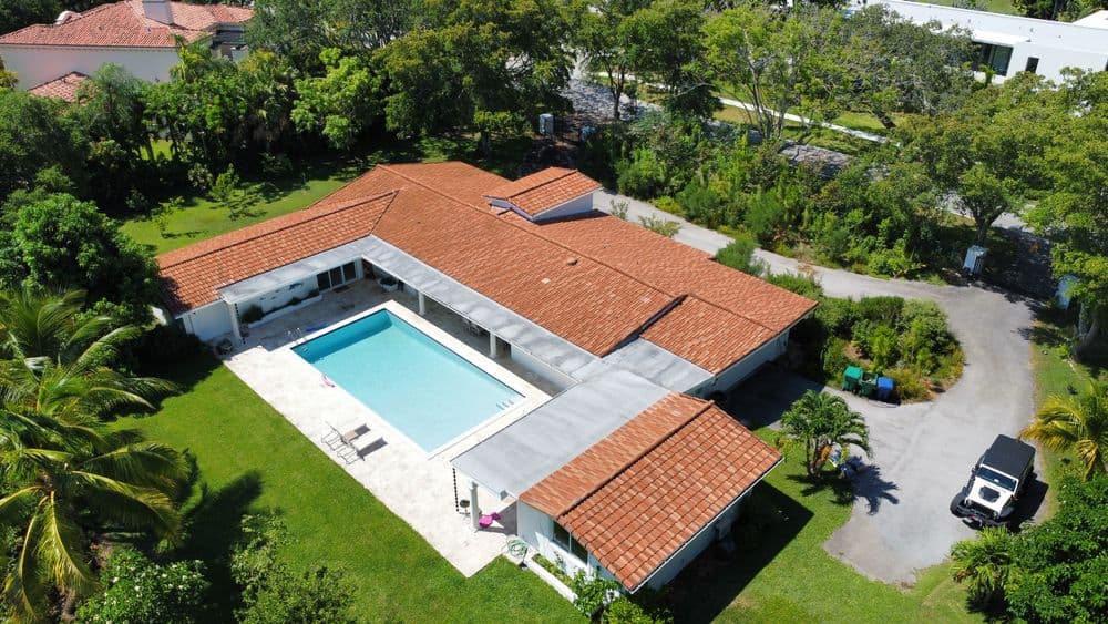 Aerial view of a modern home with a pool, surrounded by lush greenery and landscaping.