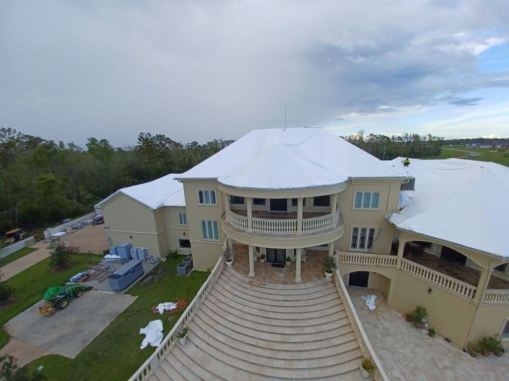 Large mansion with a covered roof, surrounded by trees and construction equipment.