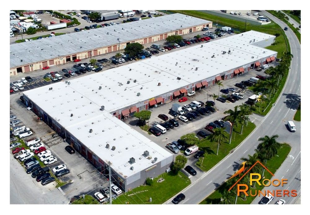 Aerial view of commercial building complex with parked cars and palm trees nearby. Roof Runners logo.