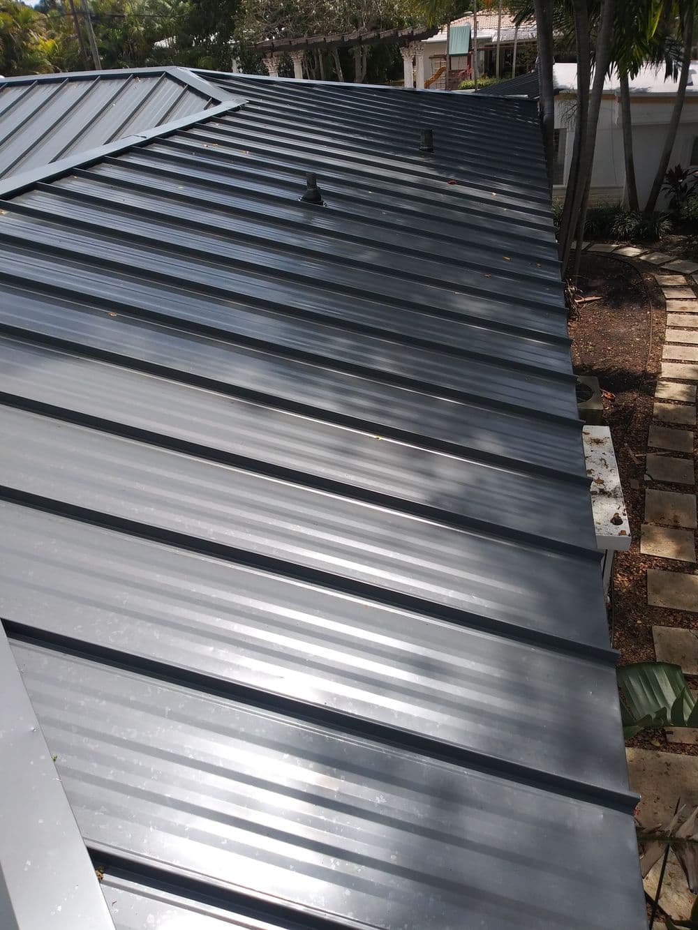 Metal roof with seam lines and ventilation, surrounded by greenery and pathways.