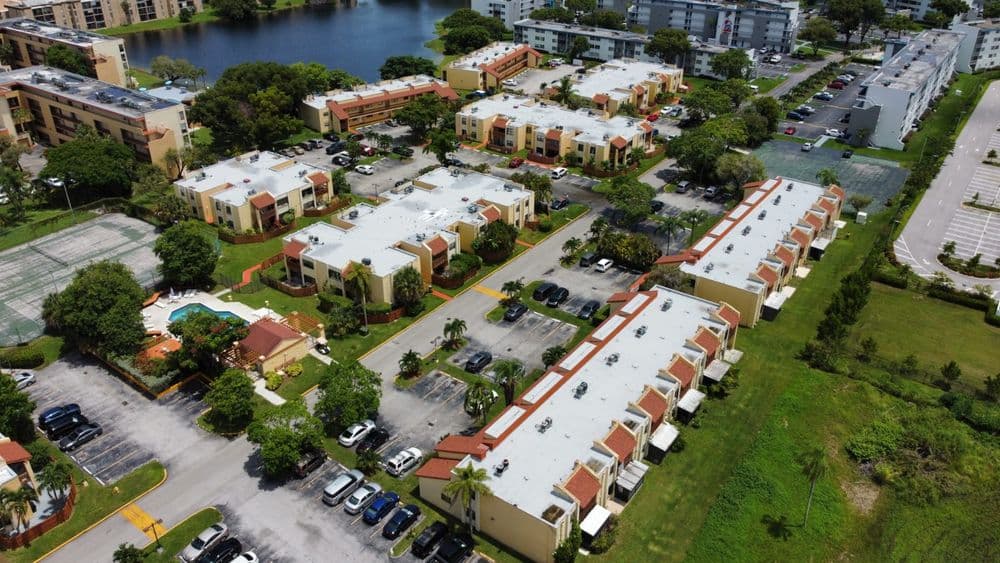 Aerial view of a residential community with apartments, parking, and a pool near a lake.