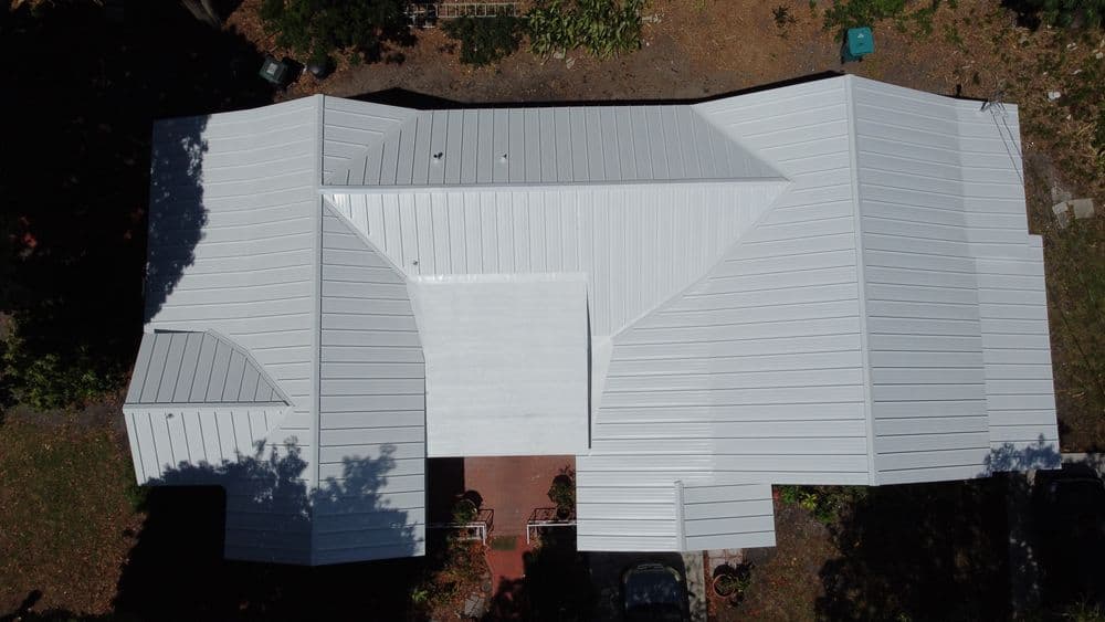 Aerial view of a modern white metal roof on a residential house surrounded by greenery.