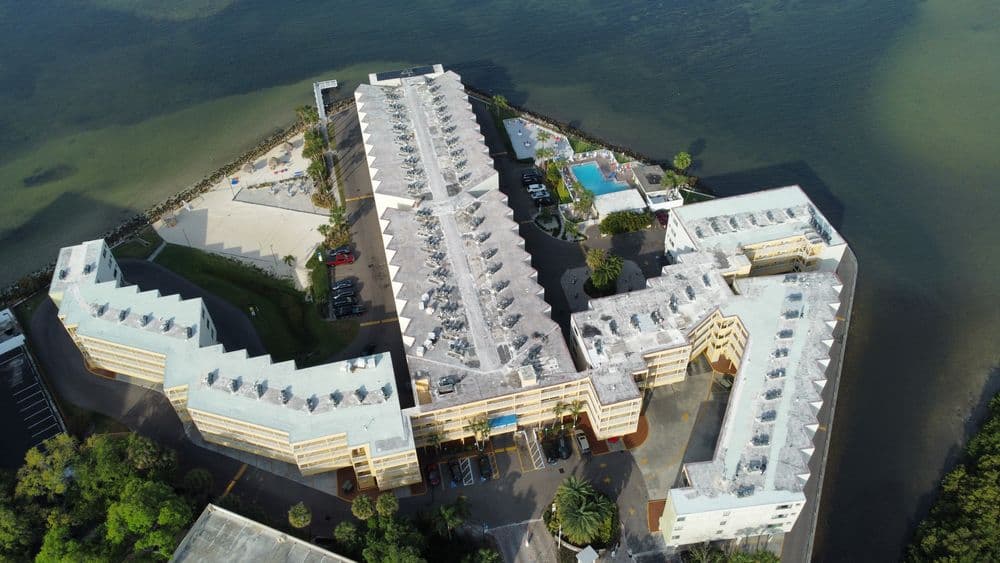 Aerial view of a beachfront hotel complex with pools and palm trees near water.