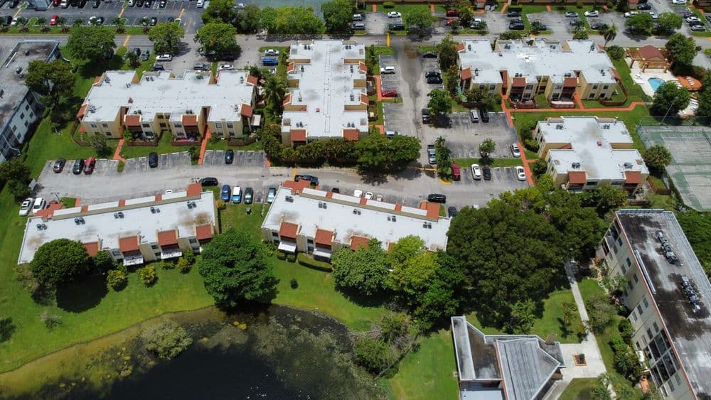 Aerial view of residential apartments surrounding a pond and parking area.