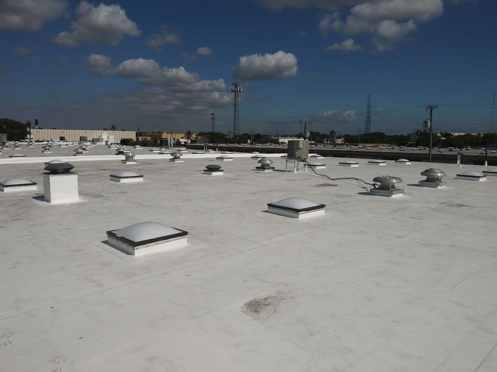 Flat commercial rooftop with ventilation units and skylights under a blue sky.