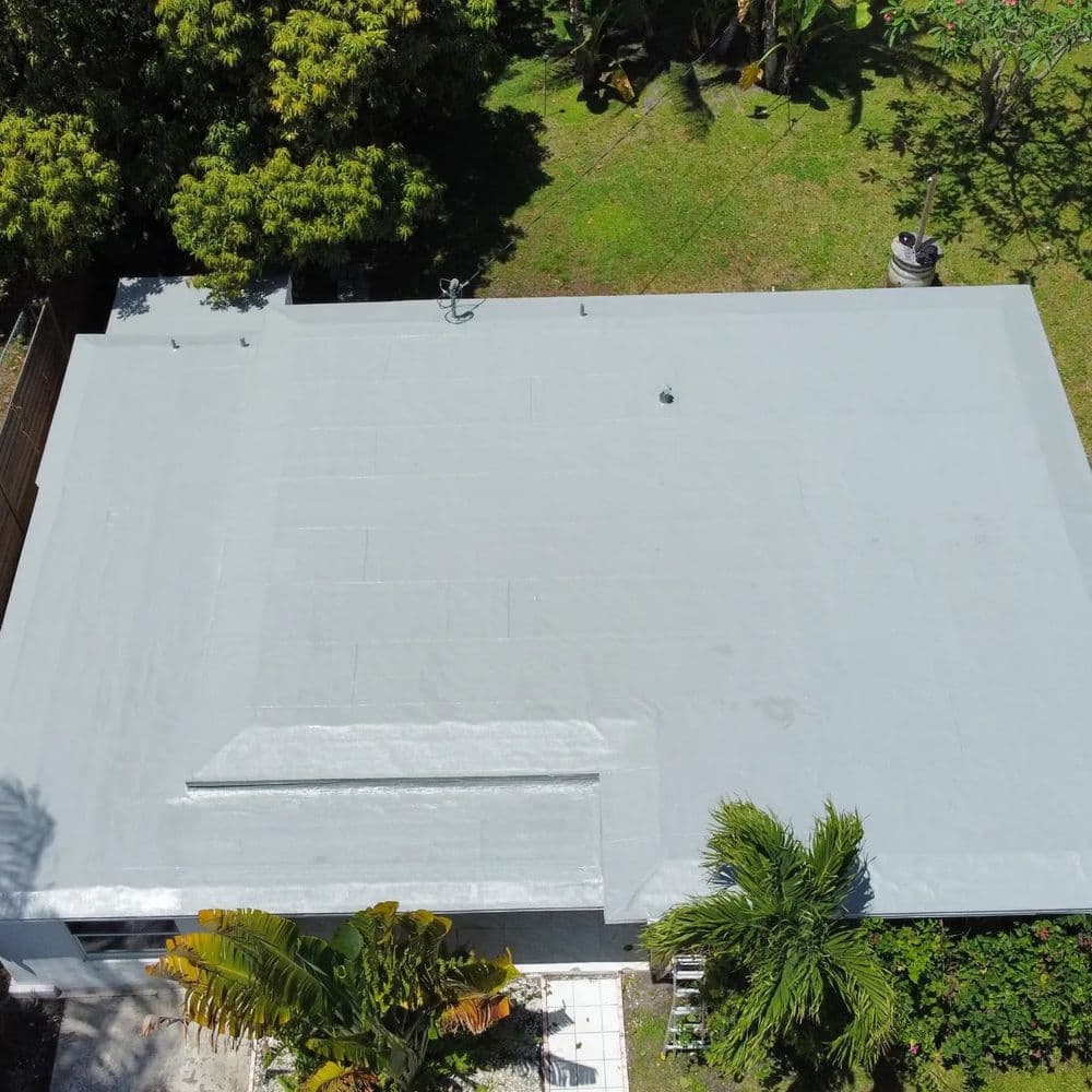 Aerial view of a newly coated gray roof surrounded by green trees and landscaping.
