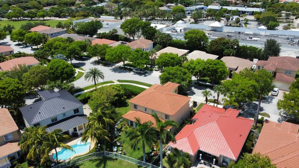 Aerial view of suburban neighborhood with houses, lush trees, and a swimming pool.