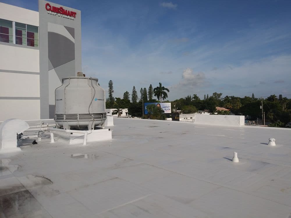 Rooftop view of a commercial building with HVAC unit and palm trees in background.