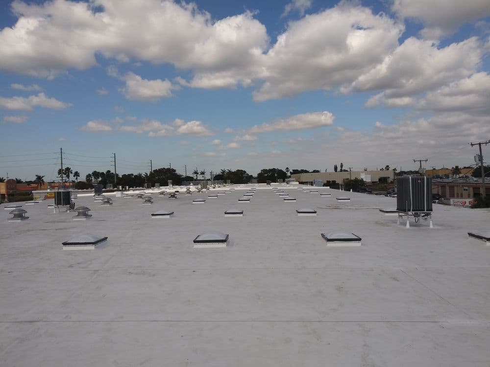 Flat commercial rooftop with ventilation units and skylights under a blue sky with clouds.