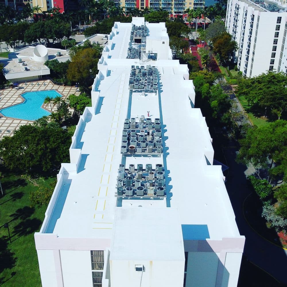 Aerial view of a building rooftop with air conditioning units and surrounding greenery.