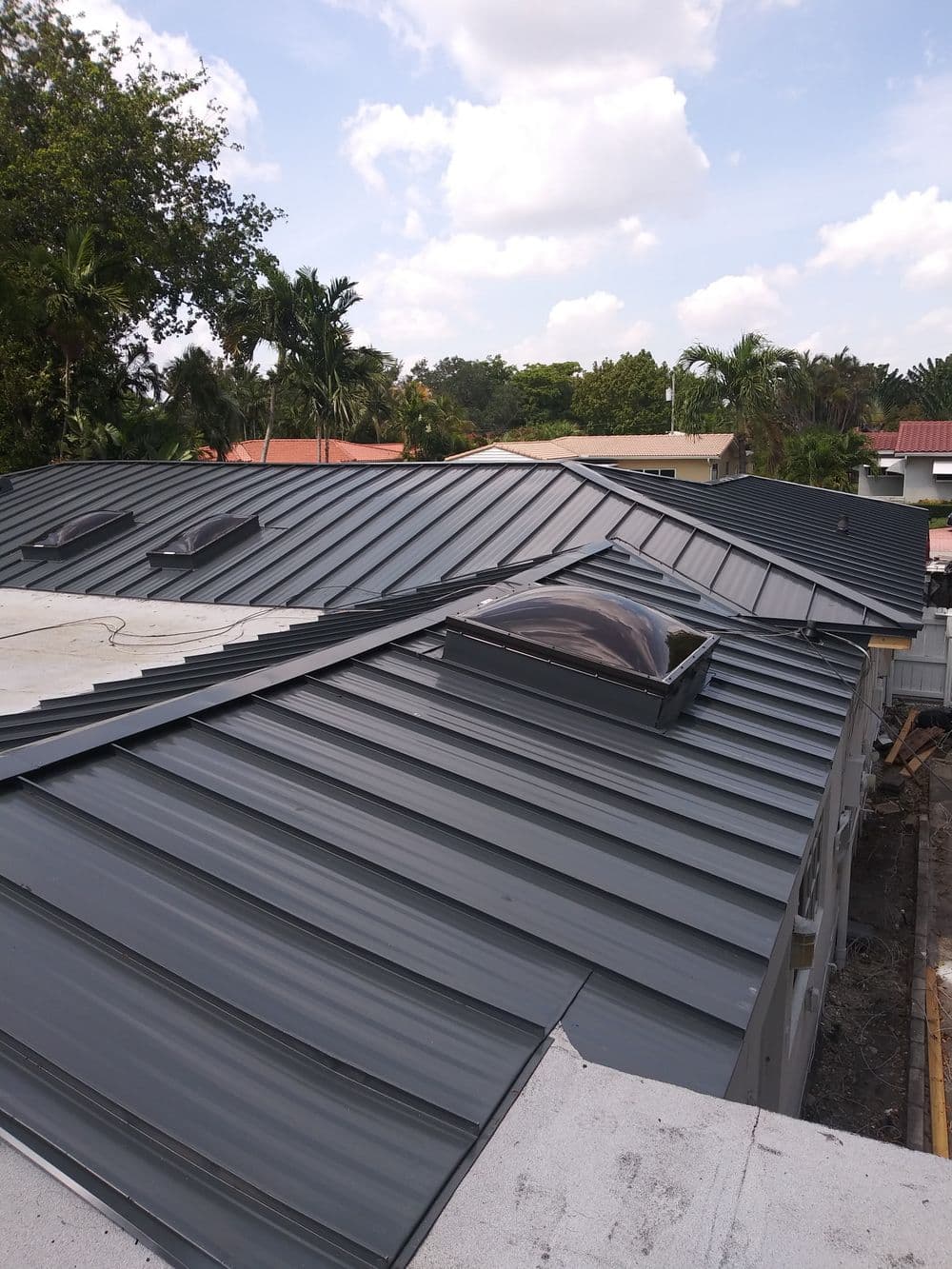 Modern metal roof installation with skylights under a bright blue sky and lush greenery.