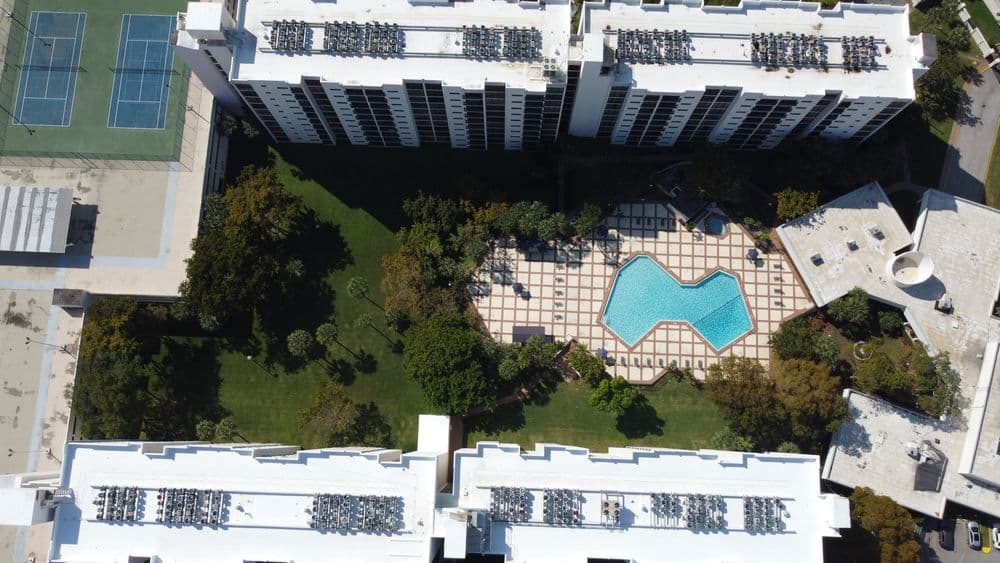 Aerial view of two high-rise buildings surrounding a pool and landscaped grounds.