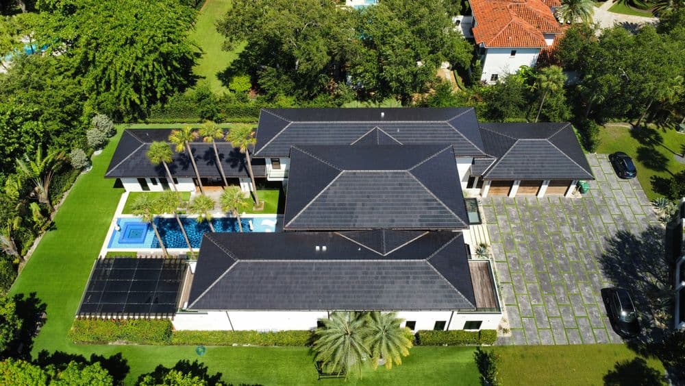 Aerial view of a luxurious home with a pool, palm trees, and landscaped lawn.