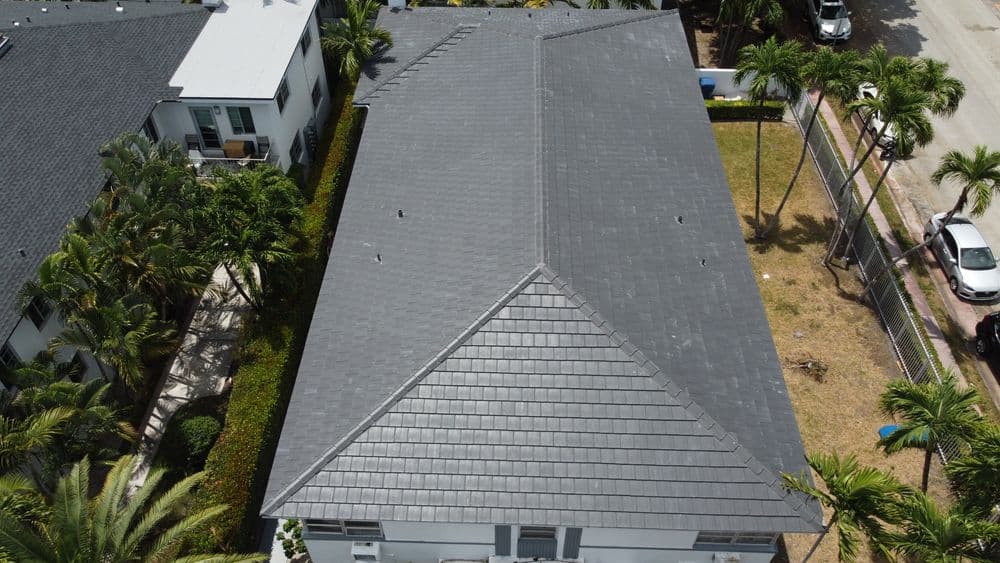 Aerial view of a modern gray roof surrounded by palm trees and green landscaping.