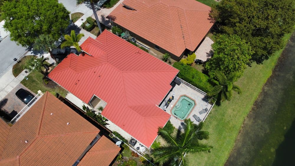 Aerial view of a home with a red tiled roof, spa, palm trees, and a nearby lake.