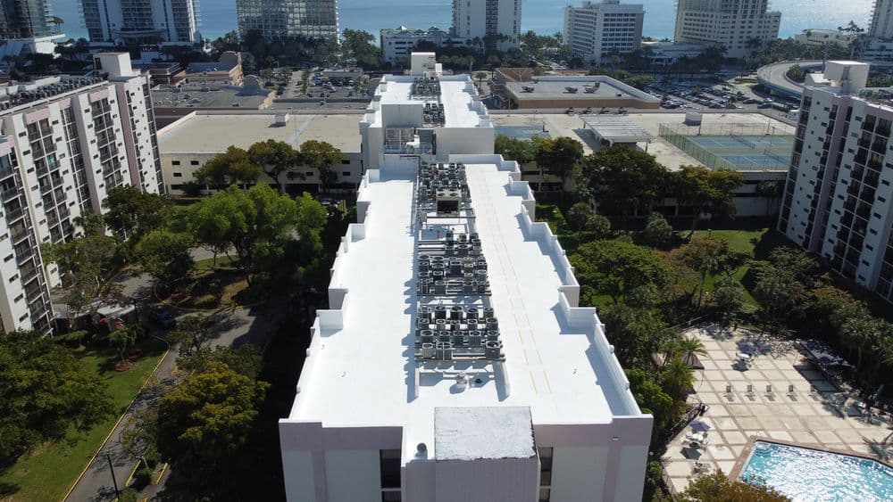 Aerial view of a residential building rooftop with HVAC units and landscaped grounds nearby.